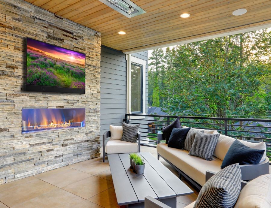 A patio with an outdoor Seura TV above a fireplace and in-ceiling speakers.