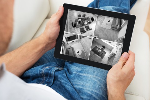 A person viewing live security camera footage of various rooms in a home on a tablet screen.