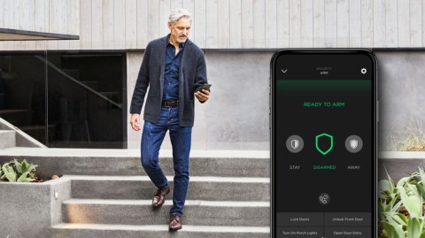 A man walks down stairs while using a smartphone to manage a Savant home security mobile app interface.