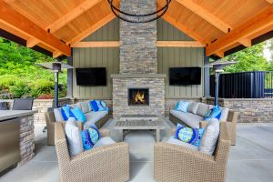 Large outdoor patio with several cushioned seating areas, a fireplace, and two TVs