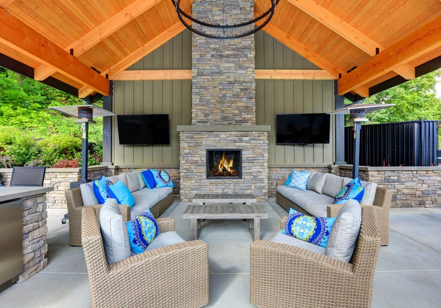 Large outdoor patio with several cushioned seating areas, a fireplace, and two TVs