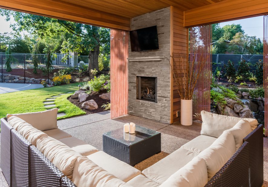 Beautiful covered patio outside new luxury home with television, fireplace, and lush green yard