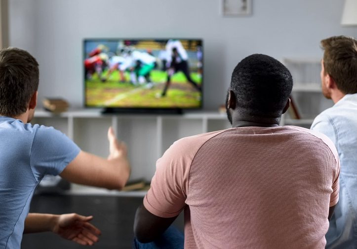 Male friends gather to watch football competition on big screen, sofa experts
