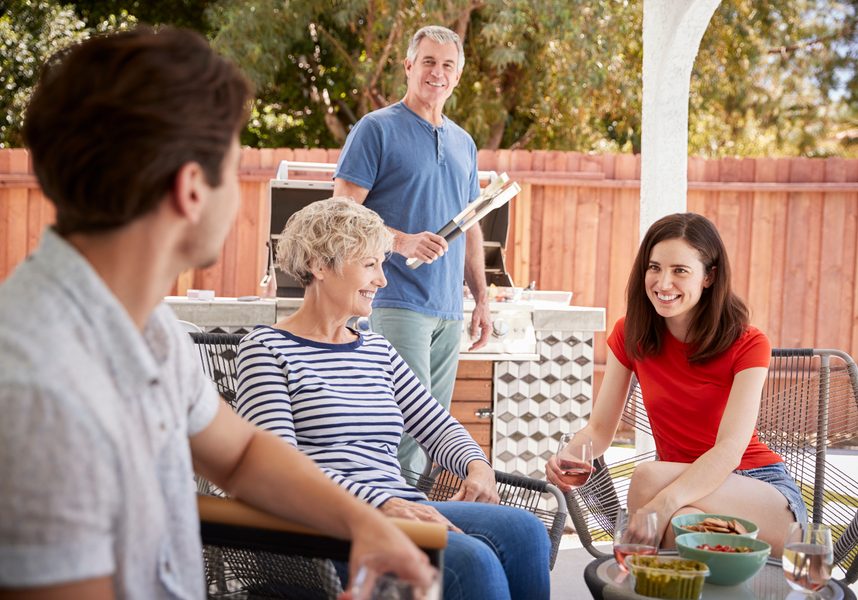 Senior couple and adult children barbecuing outside house